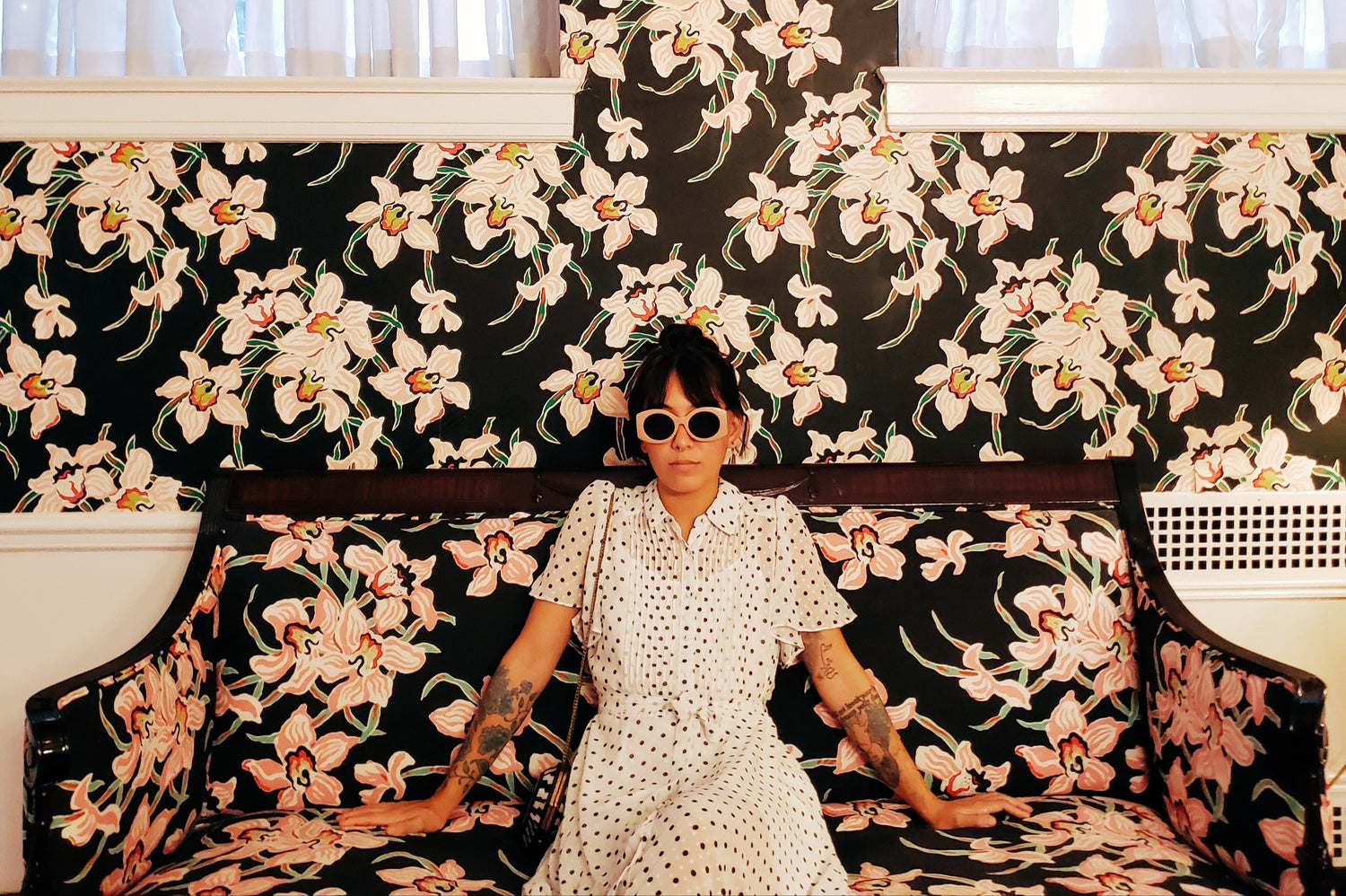 Person sitting on a floral-patterned couch with a black and white floral wall behind them.