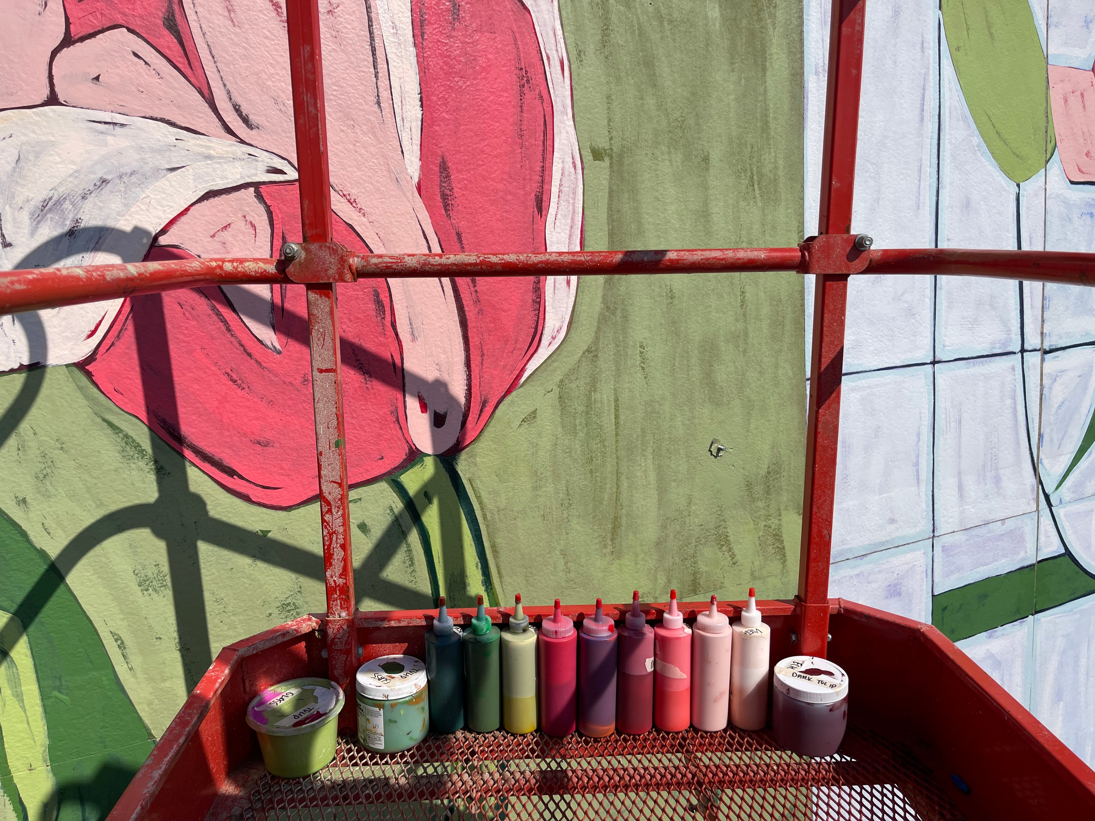 Color coded paint bottles sit on a lift near a painted mural